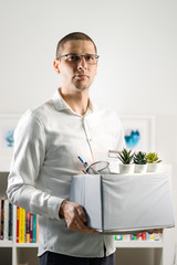 Portrait of adult caucasian man wearing white shirt holding a box personal items stuff leaving the office being fired from work due recession economic crisis downturn losing job company shutdown