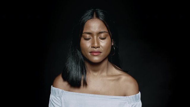 Close up of a young woman in jeans top on black background. Young dark skinned woman looking at camera.
