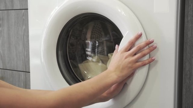 Female hand puts two WHITE SWEATERS in laundry machine. Loading washing machine. Load clothes to washer machine. Load clothes laundry washing machine. Preparing laundry washing