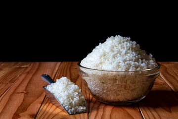 Sea salt in bowl with scoop on wooden on black background, Sea salt is salt that is produced by the evaporation of seawater. Used as a seasoning in foods, cooking, cosmetics and for preserving food..