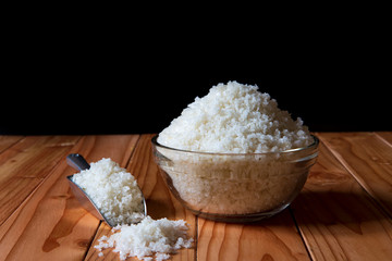Sea salt in bowl with scoop on wooden on black background, Sea salt is salt that is produced by the evaporation of seawater. Used as a seasoning in foods, cooking, cosmetics and for preserving food..