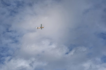 Small yellow-white plane in the clear sky with clouds.