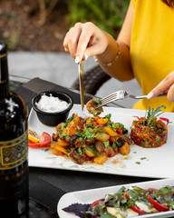 woman eating roasted meat and vegetables dish served with grilled aubergine salad