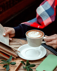 woman holding a cup of cappuccino and reading a book