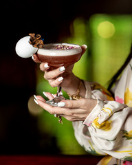 woman holding a glass of brown cocktail garnished with dried flower petals