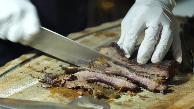 Close up on hands holding a smoked brisket on a cutting board and quickly slicing cooked beef meat into thin slices for a barbecue.