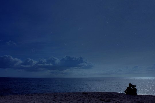 Silhouette Couple Sitting On Beach Against Sky At Night