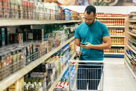 Focused African American man reading shopping list on smartphone. Responsible bearded guy buying food according to list. Shopping concept