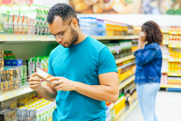 Focused African American man reading information on packaging. Concentrated bearded guy buying food...