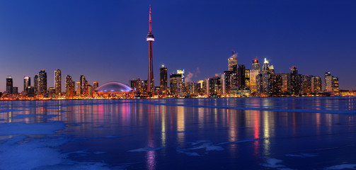 Panorama of frozen ice covered Lake Ontario reflecting the lights of Toronto city skyline at dusk