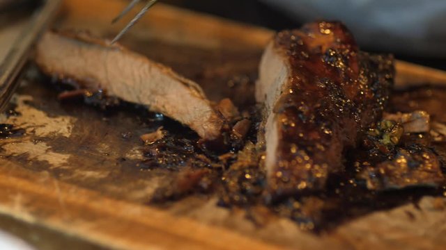 Close up on hands holding a smoked brisket on a cutting board and quickly slicing cooked beef meat into thin slices for a barbecue.