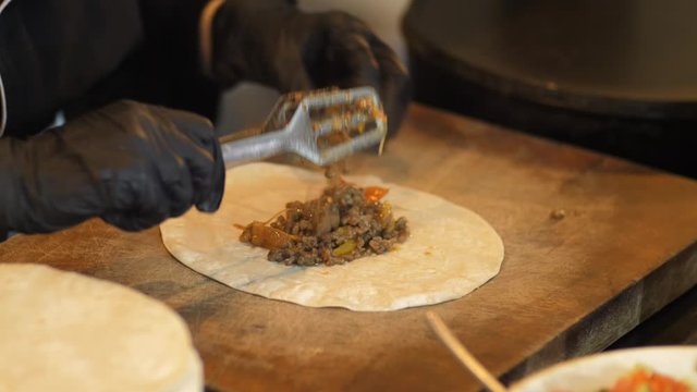 Chef cooking mexican burito at kitchen. tortilla with beef wraps meat. cooking mexican burrito. Waiter hands wrapping burrito filling in tortilla. Gourmet