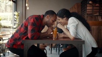 Couple drinking orange juice from one glass at a cafe. African man and woman on date sitting at cafe table and smiling.
- Powered by Adobe