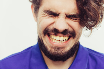 Closeup of stressed unhappy male face with pain grimace. Handsome bearded young man in blue casual t-shirt posing isolated over white background. Negative emotions concept