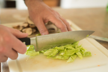 Close up of man chopping green cabbage on cutting board
