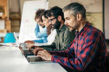 Obraz premium Startup team sitting at meeting table, using laptops. Business colleagues in casual working together in contemporary office space. Collaboration concept
