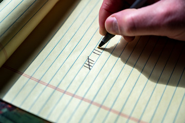 Caucasian hand using a pen to draw tally marks for counting