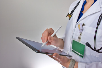 Woman using tablet in healthcare. Lady pharmacist filling out prescription information. Stethoscope over shoulder, isolated on grey background