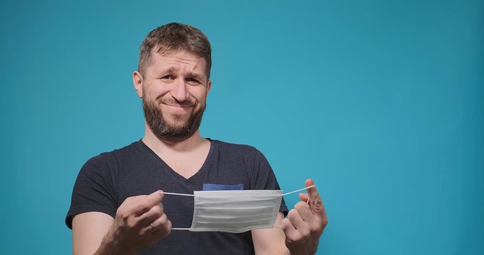 bearded guy in t-shirt looks at disposable mask in hands examining and shakes head with grimace slow motion close view