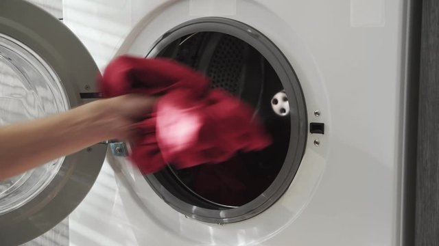 Male hand with married ring puts COLORED CLOTHES in laundry machine. Loading washing machine. Load clothes to washer machine. Load clothes laundry washing machine. Preparing laundry washing