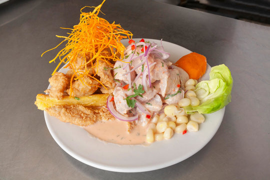 Peruvian food: fish ceviche and chicharron de pescado with fried cassava, sweet corn and sweet potato, served on a white plate
