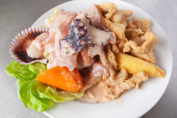 Peruvian food: fish ceviche and chicharron de pescado with fried cassava, sweet corn and sweet potato, served on a white plate