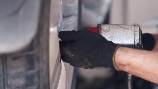 Person wears black gloves. Man is working in service center. Worker fixes automobile.