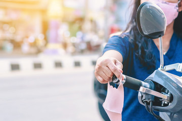Hand of woman is picking a mask that is hung on a motorcycle handle to prevent germs (Covid-19) on roadside in the city. Corona virus protection concept.