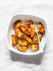Roasted new potatoes in baking dish on a light background, top view. Delicious snack, tapas