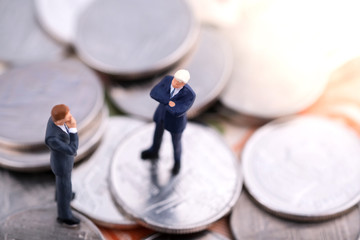 Miniature people : Top view of two businessmam standing on the coin and banknote under sunlight and discuss on the trend of stock and oil. Money, business and finance concept.
