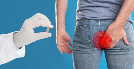 Doctor holding suppository for hemorrhoid treatment and man suffering from pain on blue background, closeup