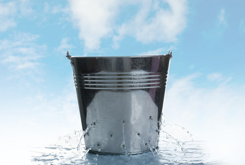 Leaky bucket with water against blue sky - obrazy, fototapety, plakaty