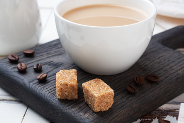 A Cup of coffee with milk and cubes of cane sugar on a wooden stand. Background of white rustic boards. Copy space.