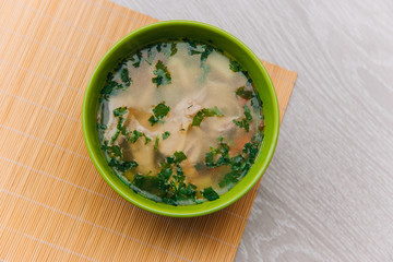 Green plate with noodle soup. With poultry meat on a light wooden table. Dietary Chicken Soup. Healthy eating
