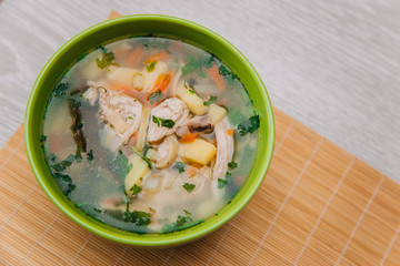 Green plate with noodle soup. With poultry meat on a light wooden table. Dietary Chicken Soup. Healthy eating