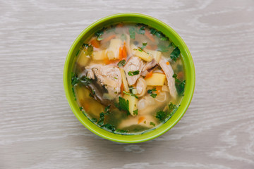 Green plate with noodle soup and half an egg on a light wooden table. Diet soup. Healthy eating