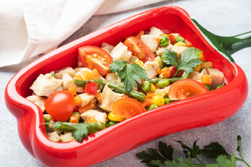 Stewed chicken meat with vegetables carrots peppers peas corn in a plate in the form of red pepper. Copy space.