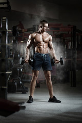 Fototapeta na wymiar Athlete muscular bodybuilder in gym training biceps with dumbbell