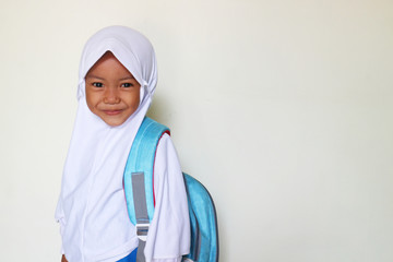 A child wears a white school uniform and wears a hijab and a bag with white background - added text