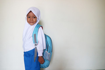 A child wears a white school uniform and wears a hijab and a bag with white background - added text