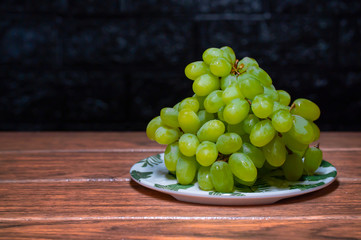 uvas verdes frescos sobre un plato blanco y sobre un fondo negro