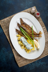 Fried smelt served on a white plate with potatoes, sauce and onions