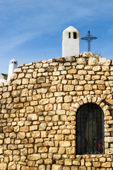 Fototapeta na wymiar beautiful old stone cave church with white chimneys and cross on the roof in guadix spain with blue sky on the background