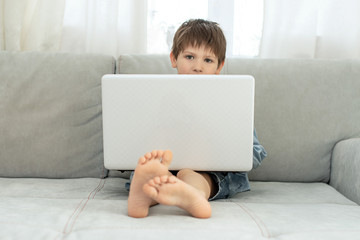 Naklejka premium Kids and gadgets. Distance learning during isolation during quarantine in coronavirus. Boy and laptop at home. Lifestyle