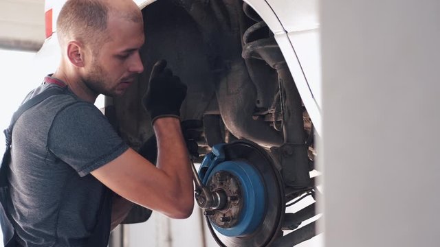 Man repairs white car. Machine is without wheels. Worker is fixing car in service center.