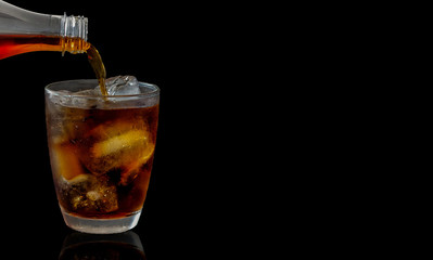 Cola soft drinks are poured from black background bottles.