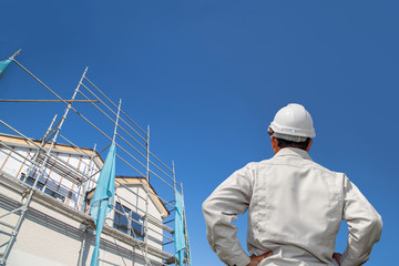 建設中の戸建て住宅を見る作業着姿の男性の後ろ姿。