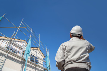 建設中の戸建て住宅を見る作業着姿の男性の後ろ姿。
