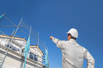 建設中の戸建て住宅を見る作業着姿の男性の後ろ姿。