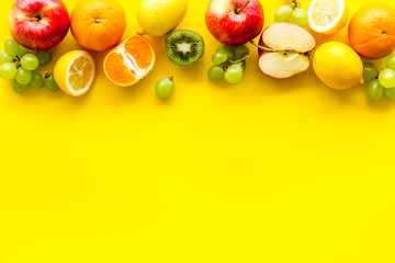 Fresh fruits background with citruses, apple, kiwi and grape on yellow table top-down frame copy space